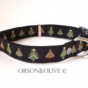 Op de afbeelding: Zwarte hondenriem met een herhalend patroon van groene kerstboompjes op een zwarte achtergrond. De riem heeft een zilveren gesp en een zilveren D-ring.