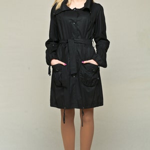 May include: A black long-sleeved jacket with a high collar, a belt, and two pockets. The jacket is belted at the waist and has a drawstring at the bottom.