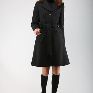 May include: A black belted coat with a mock neck collar. The coat is knee-length and has a fitted silhouette.