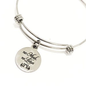 May include: Silver bangle bracelet with a round charm that reads "no mud, no lotus" and a lotus flower design.