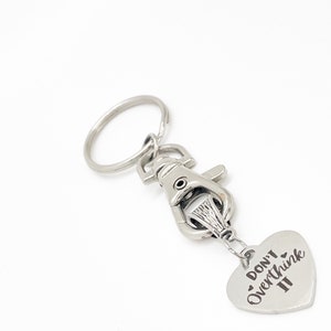 May include: Silver keychain with a heart-shaped charm that says "Don't Overthink It". The charm is attached to a silver lobster clasp and a silver key ring.