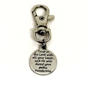 May include: Silver keychain with a round charm that reads "Trust in the Lord with all your heart... and He will direct your paths. Proverbs 3:5,6"