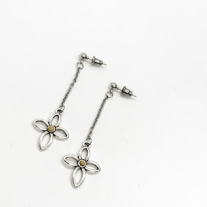 May include: A pair of silver dangle earrings with a small gold flower charm at the end of each chain.