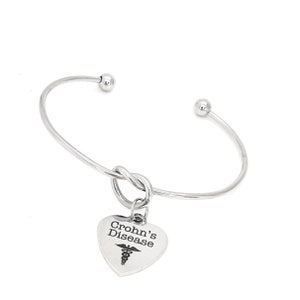 May include: Silver bangle bracelet with a knot design and a heart charm that says "Crohn's Disease" with a medical symbol.