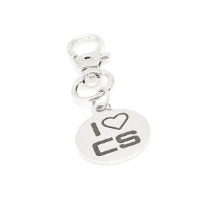 以下が含まれることがあります： 「I ♥ CS」と書かれた丸いチャームが付いたシルバーのキーホルダーです。