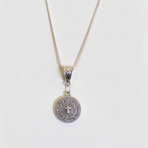 May include: A silver chain necklace with a round pendant that reads "Be still and know that I am God". The pendant features a small cross in the center.