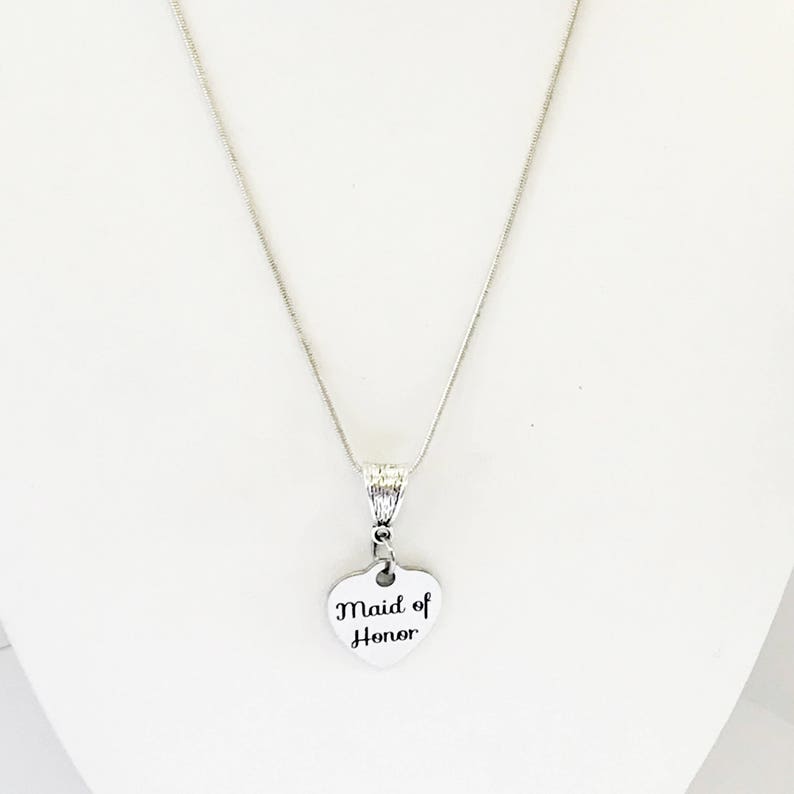 Puede incluir: Collar de plata con un colgante en forma de coraz&oacute;n que dice "Maid of Honor".