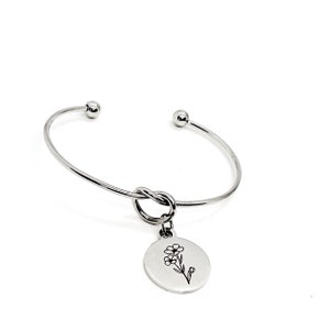 May include: A silver bangle bracelet with a knot detail and a charm featuring a delicate flower design.