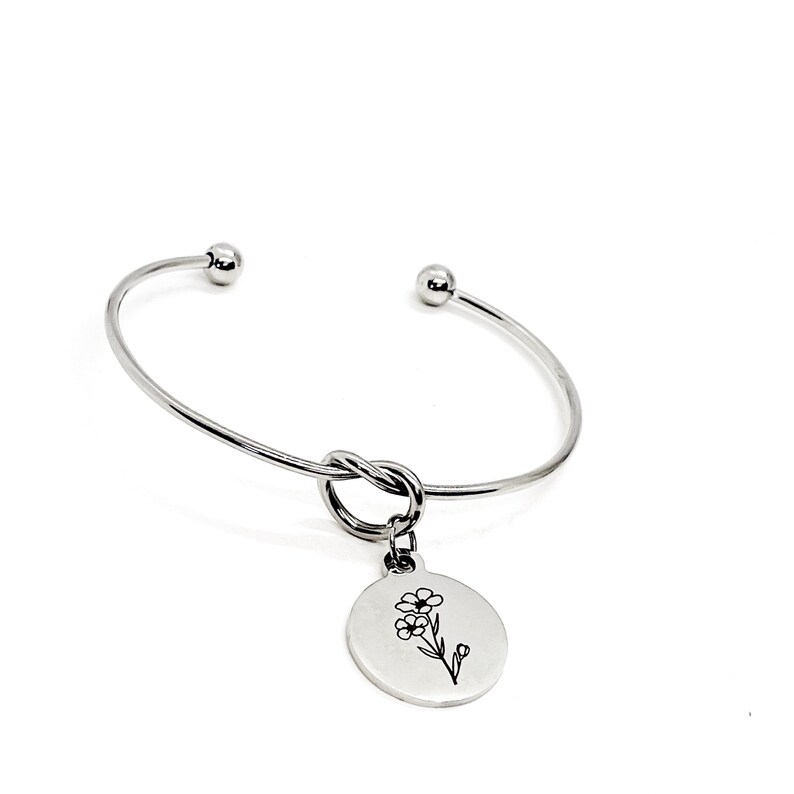 May include: A silver bangle bracelet with a knot detail and a charm featuring a delicate flower design.