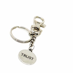 May include: Silver keychain with a round charm that says "TRUST" on it.
