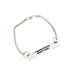 Puede incluir: Un brazalete de cadena de plata con un dije de barra de plata que dice "Respetuosamente no me importa."