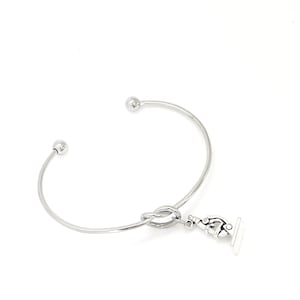 Puede incluir: Pulsera de brazalete de plata con un diseño de nudo y un dije de microscopio.