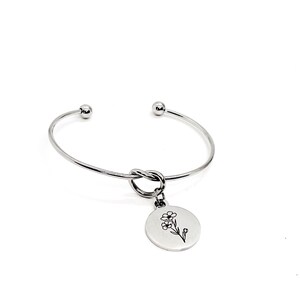 May include: A silver bangle bracelet with a knot detail and a charm featuring a delicate flower design.