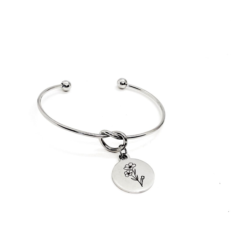 May include: A silver bangle bracelet with a knot detail and a charm featuring a delicate flower design.