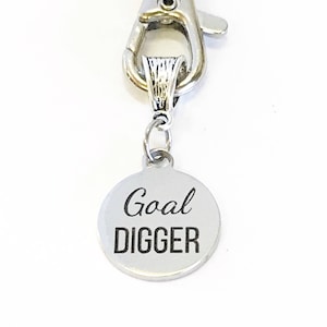 May include: Silver keychain with a round metal charm that says "Goal Digger" in black lettering.