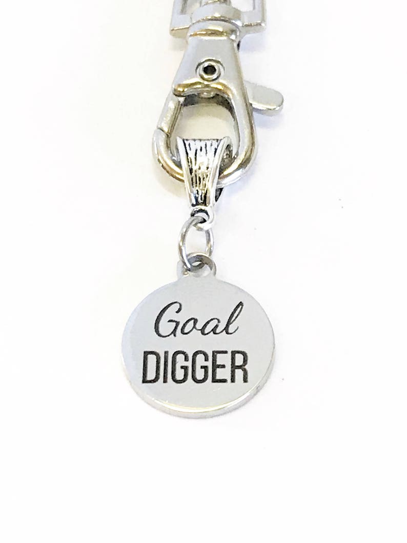 May include: Silver keychain with a round metal charm that says "Goal Digger" in black lettering.