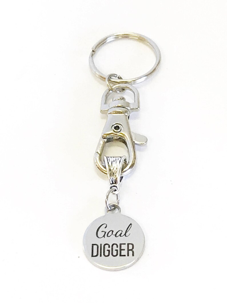 May include: Silver keychain with a silver clip and a round silver charm that says "Goal Digger" in black lettering.