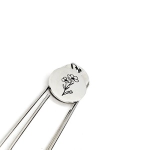 May include: Silver bookmark with a round charm featuring a simple line drawing of a flower.