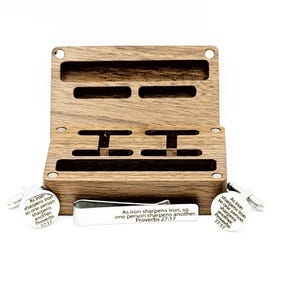 May include: A wooden box with compartments for cufflinks and a tie clip. The set includes silver cufflinks and a tie clip, each with the text "As iron sharpens iron, so one person sharpens another. Proverbs 27:17."
