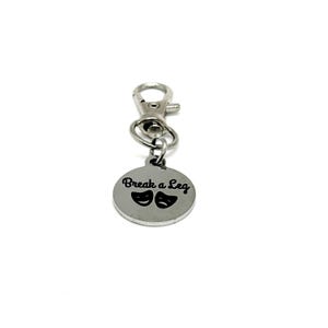 May include: A silver-colored keychain with a round charm. The charm has the phrase "Break a Leg" and two theater masks. The keychain has a lobster clasp for easy attachment.