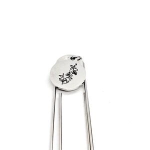 May include: Silver bookmark with a round charm featuring a floral design and the word "love" engraved on it.