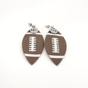 May include: A pair of brown leather football-shaped earrings with white stitching and silver charms that say "#12".