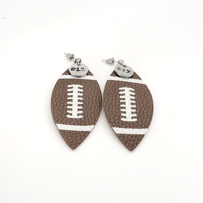 May include: A pair of brown leather football-shaped earrings with white stitching and silver charms that say "#12".