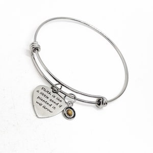 Puede incluir: Pulsera extensible de plata con un dije en forma de corazón que dice "Faith is like a little seed if planted it will grow". El dije está unido a un pequeño dije redondo con una piedra marrón.
