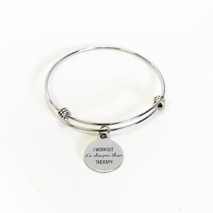 May include: Silver expandable bangle bracelet with a round charm that reads "I workout it's cheaper than therapy".