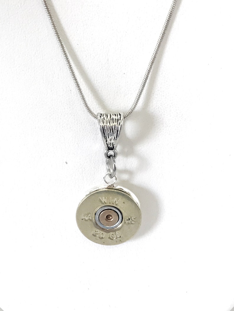 May include: A silver chain necklace with a silver pendant featuring a 20 gauge shotgun shell casing. The casing has the text "WIN" and "HS" on it.