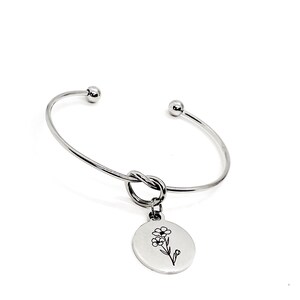 May include: A silver bangle bracelet with a knotted design and a charm featuring a delicate flower etched on a round disc.