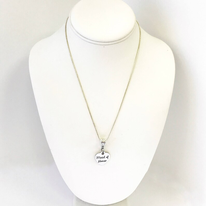 Puede incluir: Un collar de plata con un colgante en forma de coraz&oacute;n que dice "Maid of Honor".