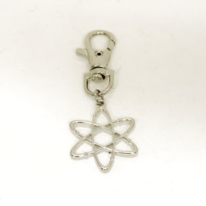 May include: Silver atom keychain with a silver clip. The atom is a stylized representation of an atom with a nucleus and orbiting electrons.