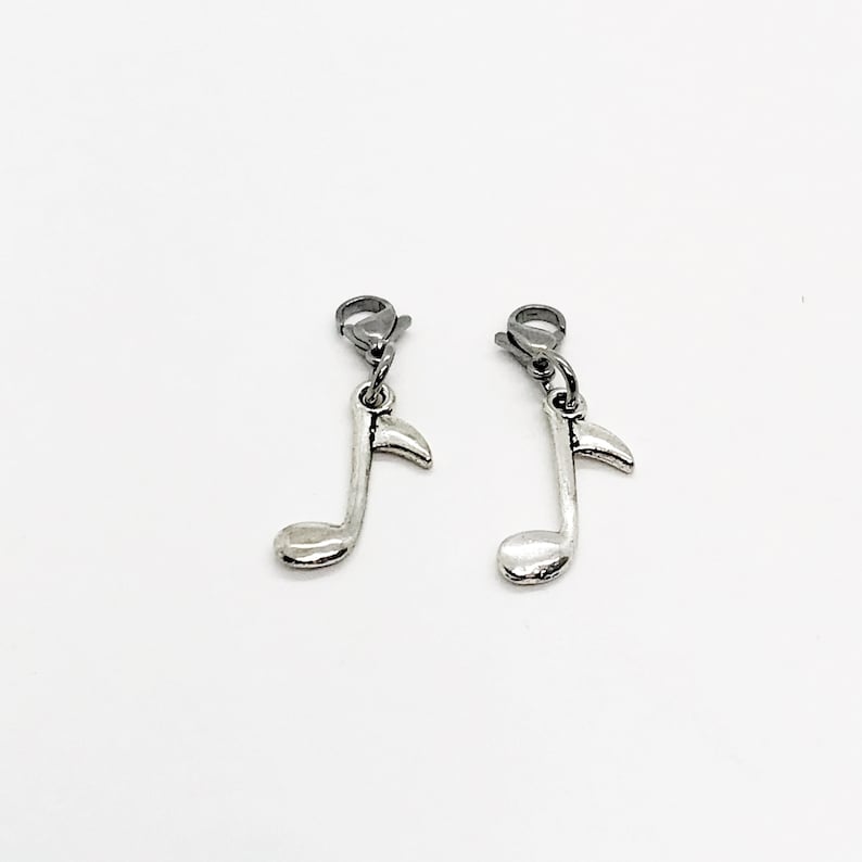 Pode incluir: Dois pingentes de prata em forma de nota musical com um fecho de lagosta de prata. Os pingentes est&atilde;o pendurados nos fechos.