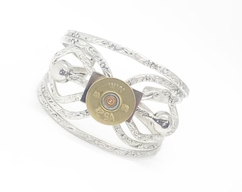 May include: Silver ring with a woven design and a brass bullet casing in the center. The bullet casing has the text "WIN 12 GA 2 3/4" printed on it.