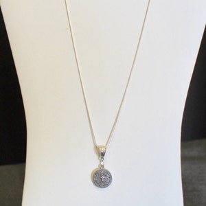 May include: A silver chain necklace with a round pendant featuring a cross and the words "Pray for us" inscribed around it.