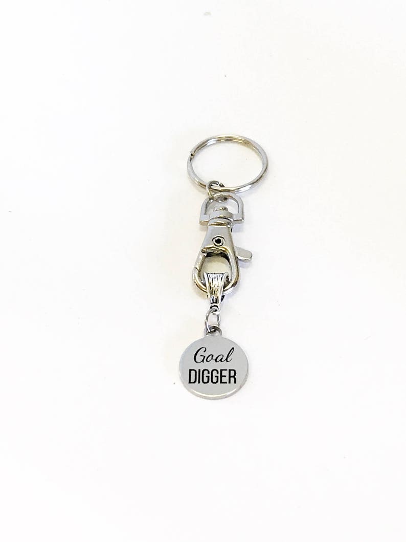 May include: Silver keychain with a silver clip and a round silver charm that says "Goal Digger" in black lettering.