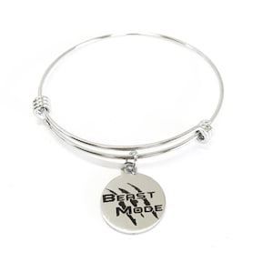 Op de afbeelding: Een zilveren armband met een ronde bedel waarop in zwarte letters "Beast Mode" staat met een klauwmotief.