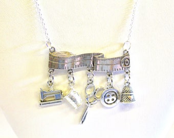 May include: A silver necklace with a measuring tape charm and several other charms, including a sewing machine, spool of thread, scissors, button, and thimble.