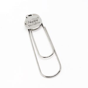 May include: Silver bookmark with a round charm that says "Think Happy Thoughts".