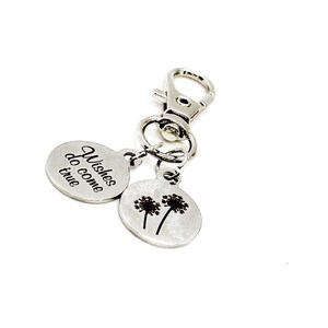 May include: Silver keychain with two charms. One charm has the text "Wishes do come true" and the other charm has a silhouette of two dandelions.