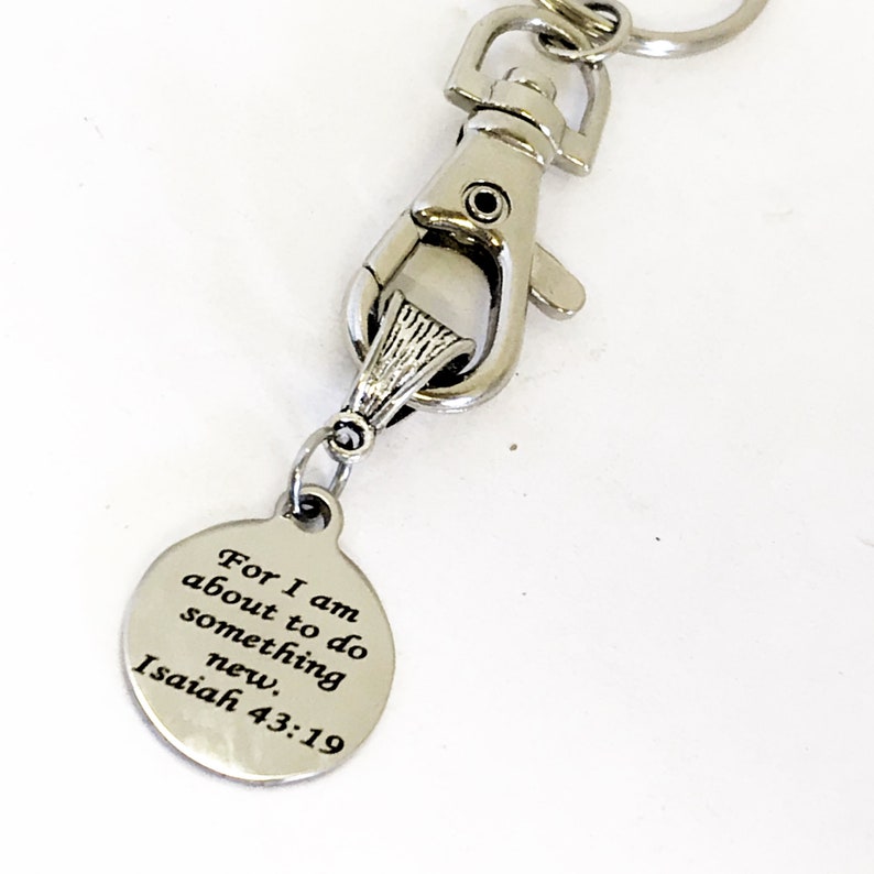 May include: Silver keychain with a round charm that says "For I am about to do something new. Isaiah 43:19"