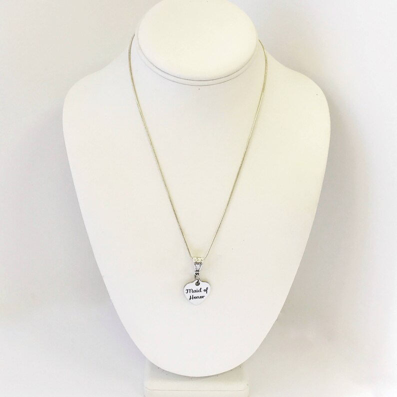 Puede incluir: Collar de plata con un colgante en forma de coraz&oacute;n que dice "Maid of Honor".