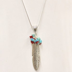 May include: Silver-toned feather pendant necklace with a delicate chain. The pendant features a detailed feather design, accented with clusters of red and turquoise-colored stones. A stylish accessory.