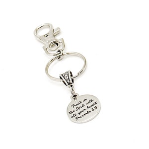Può includere: Portachiavi d'argento con un ciondolo rotondo che dice "Trust in the Lord with all your heart Proverbs 3:5".