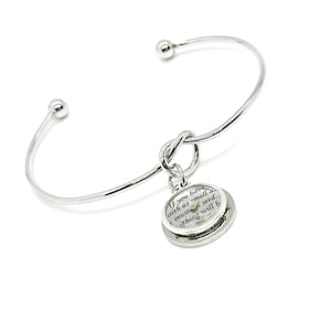 May include: A silver-colored bangle bracelet with a knot design and a round charm. The charm has a small seed and text that reads, "If you have faith as small as a mustard seed...nothing will be impossible for you."
