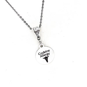 Puede incluir: Collar de plata con un colgante redondo que dice "Codeine Allergy" con un símbolo médico.
