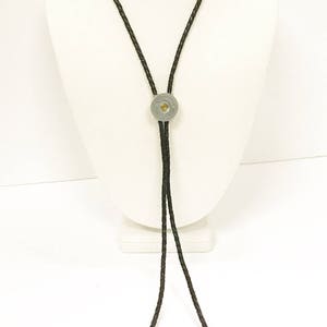 May include: A black leather bolo tie with a silver bullet casing as the centerpiece. The tie is displayed on a white mannequin.