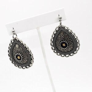 Puede incluir: Un par de pendientes de plata con un dise&ntilde;o de filigrana y una peque&ntilde;a perla dorada en el centro. Los pendientes tienen forma de l&aacute;grima y un dise&ntilde;o delicado e intrincado.