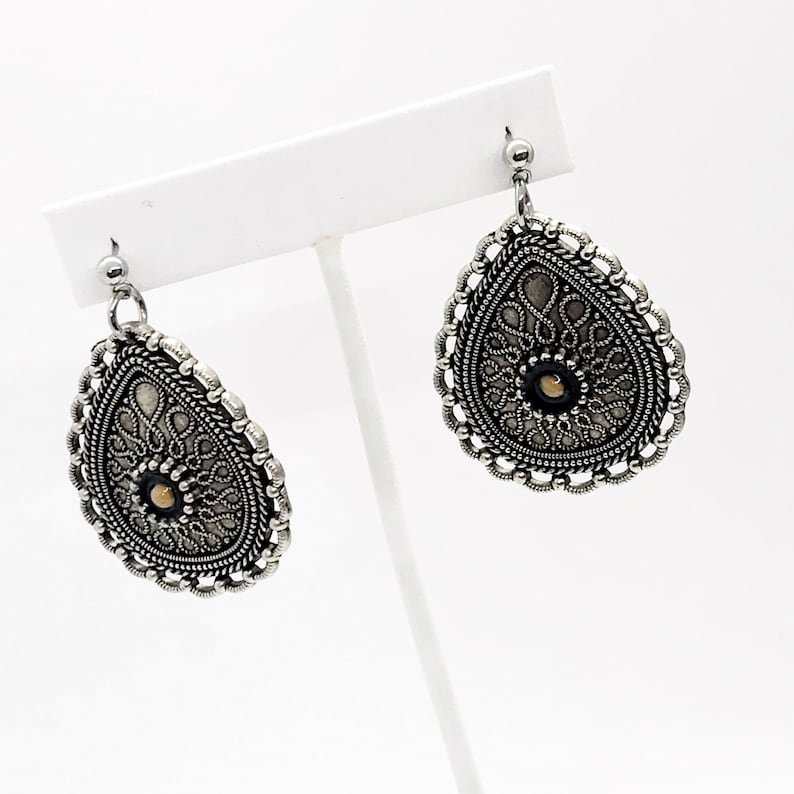 Puede incluir: Un par de pendientes de plata con un dise&ntilde;o de filigrana y una peque&ntilde;a perla dorada en el centro. Los pendientes tienen forma de l&aacute;grima y un dise&ntilde;o delicado e intrincado.